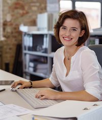 Frau sitzt lächelnd am Schreibtisch vor PC