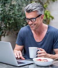 Mann sitzt mit Kaffetasse am Laptop